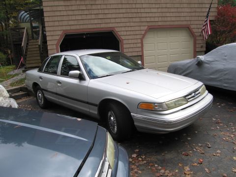 1991 Ford LTD Crown Victoria - Silver sedan parked in front of a garage with an American flag visible.