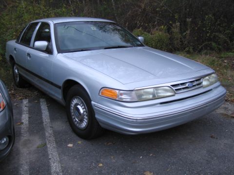1991 Ford LTD Crown Victoria - A silver sedan is parked in a lot, showing its front 3/4 view with chrome wheels and bumper trim.