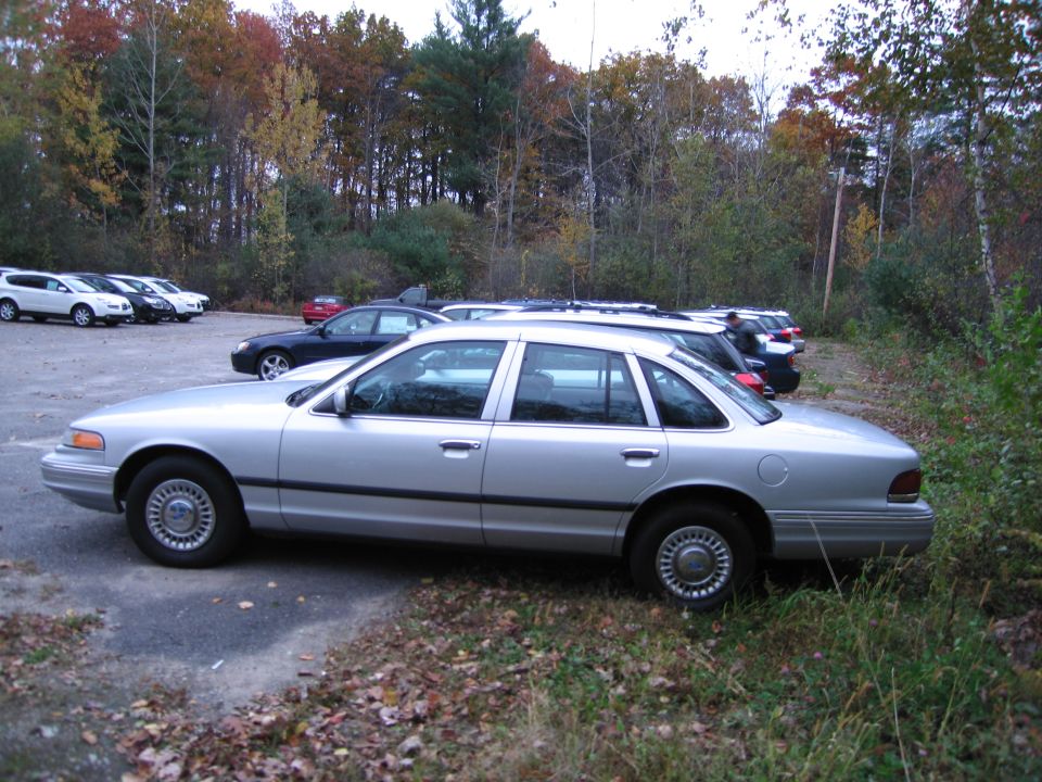 1991 Ford Crown Victoria LTD parked on asphalt with grass and trees in background. Other cars are visible