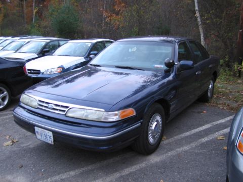 1991 Ford LTD Crown Victoria - A dark blue Ford Crown Victoria Police Interceptor is parked in a lot with other vehicles visible.