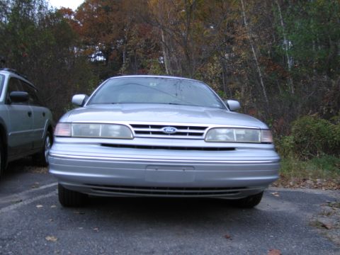1991 Ford LTD Crown Victoria - A silver Ford Crown Victoria LTD is parked in front of a wooded area during the fall.