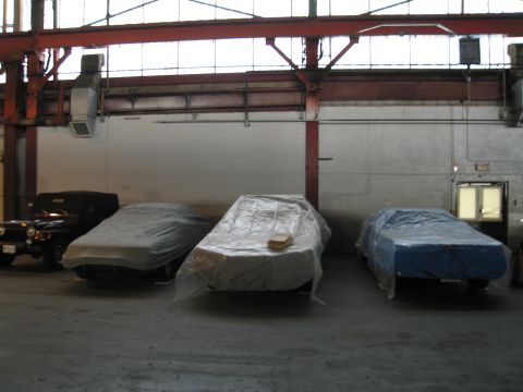 1991 Ford LTD Crown Victoria - Several vehicles are covered in protective sheeting inside a large industrial space.