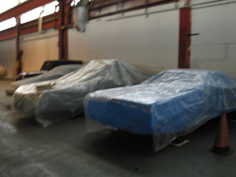 1991 Ford LTD Crown Victoria - Several vehicles are covered in protective sheeting inside a warehouse, awaiting their next phase.