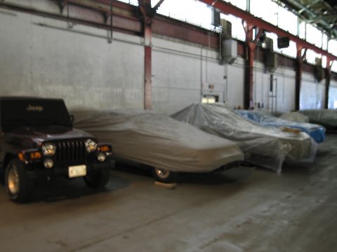 1991 Ford LTD Crown Victoria - A Jeep Wrangler is parked in a warehouse alongside several other vehicles covered with protective tarps.