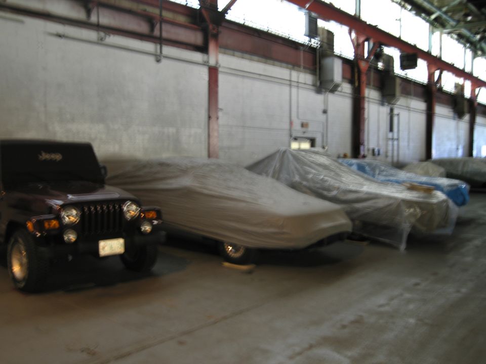 Jeep Wrangler parked in front of multiple cars covered with tarps inside a warehouse