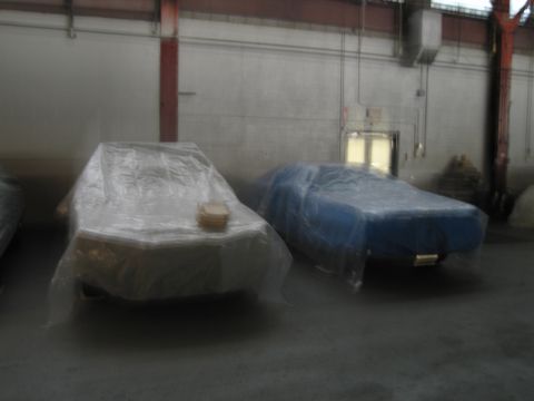 1991 Ford LTD Crown Victoria - Two vehicles are covered in plastic sheeting in a dimly lit indoor storage area.