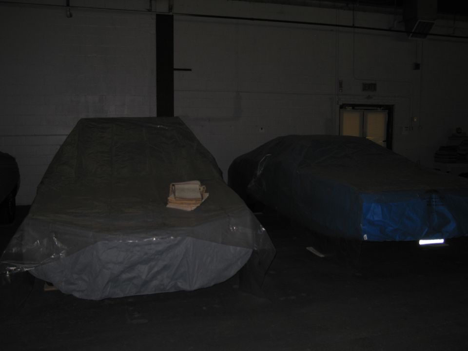 Two cars covered in tarps inside a dark garage