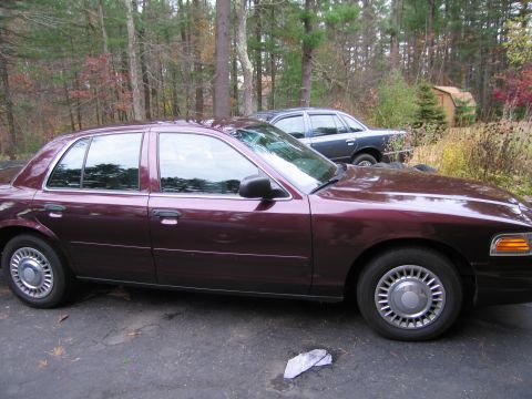1991 Ford LTD Crown Victoria - Two sedans, a maroon 1991 Ford Crown Victoria LTD and a dark sedan, are parked on asphalt with trees in the background.