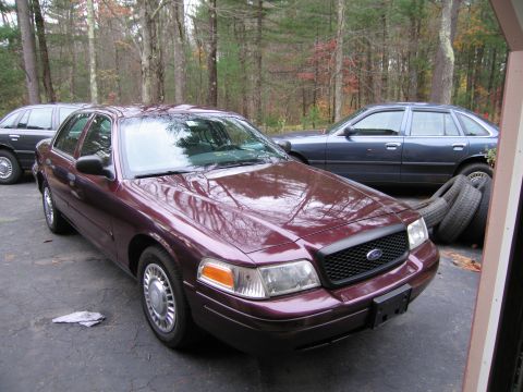 1991 Ford LTD Crown Victoria - A maroon Ford Crown Victoria is parked in a driveway with another car behind it and tires stacked to the side.