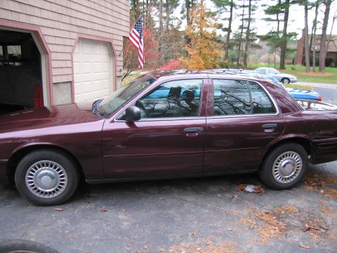1991 Ford LTD Crown Victoria - Side view of a maroon sedan parked in a driveway with a garage and trees in the background. Another vehicle is parked further down the driv…