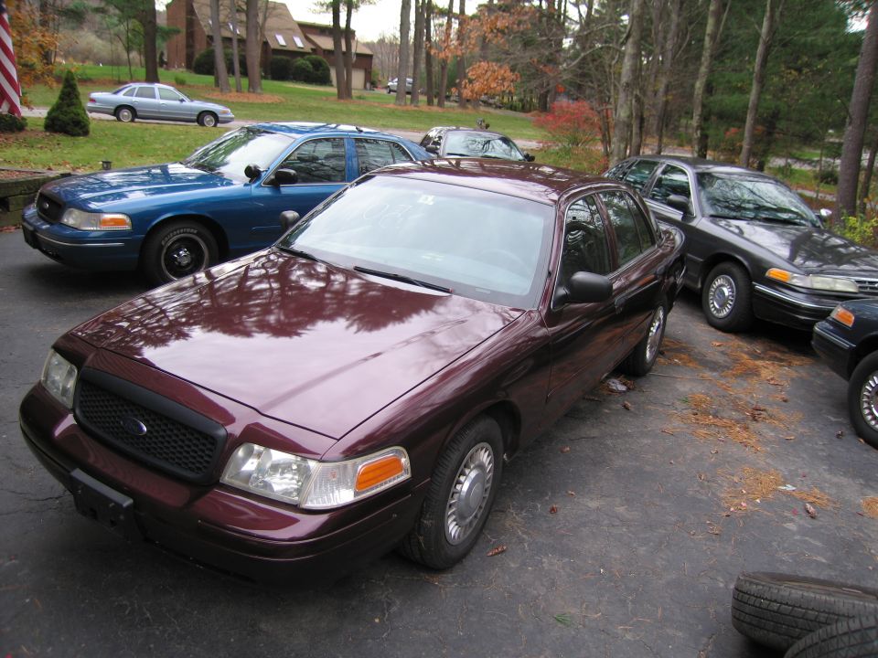 Maroon Ford Crown Victoria in foreground, blue and dark gray Crown Victorias behind it