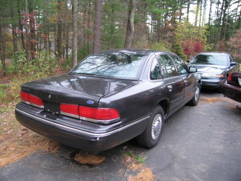 1991 Ford LTD Crown Victoria - A dark gray sedan is parked on an asphalt surface, with other vehicles visible behind it.