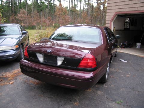 1991 Ford LTD Crown Victoria - A maroon sedan is parked in a driveway next to another sedan, with a garage in the background.