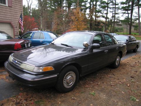 1991 Ford LTD Crown Victoria - Three sedans are parked in a driveway on a cloudy day.