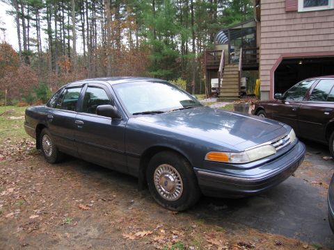 1991 Ford LTD Crown Victoria - A blue Ford Crown Victoria is parked in front of a house with trees in the background. Another vehicle is partially visible in the garage.