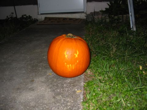 1997 Ford Crown Victoria - A carved pumpkin sits on a concrete walkway in front of a door.