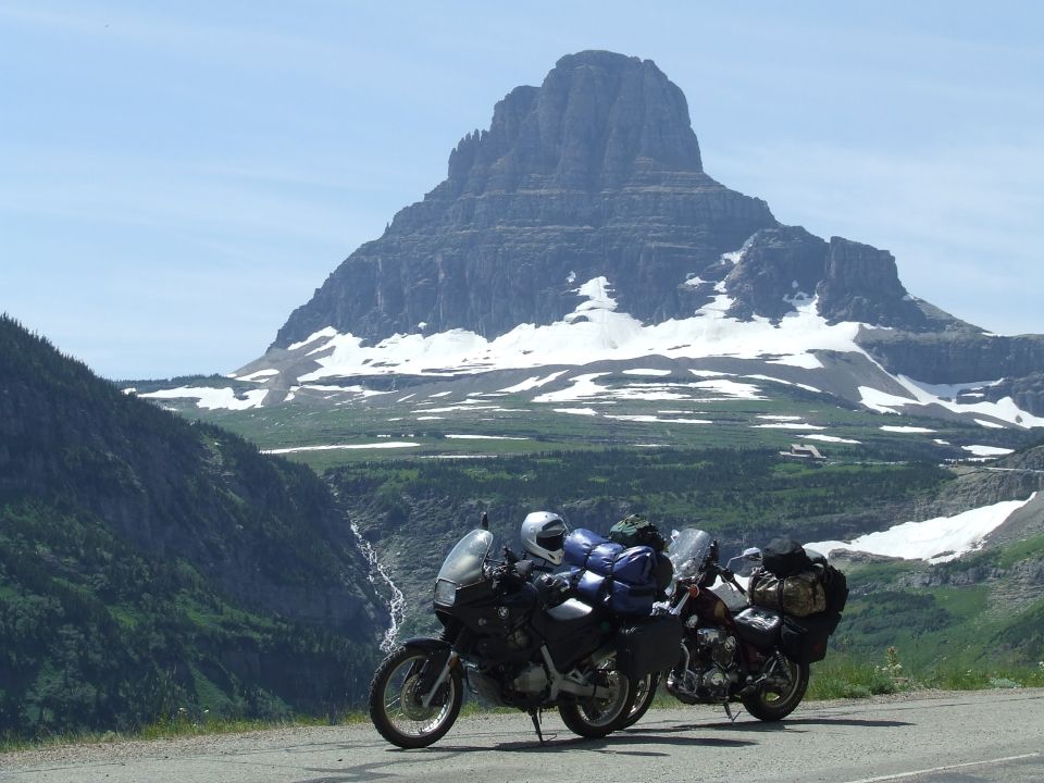 Two motorcycles parked on a road with a large, snow-capped mountain in the background