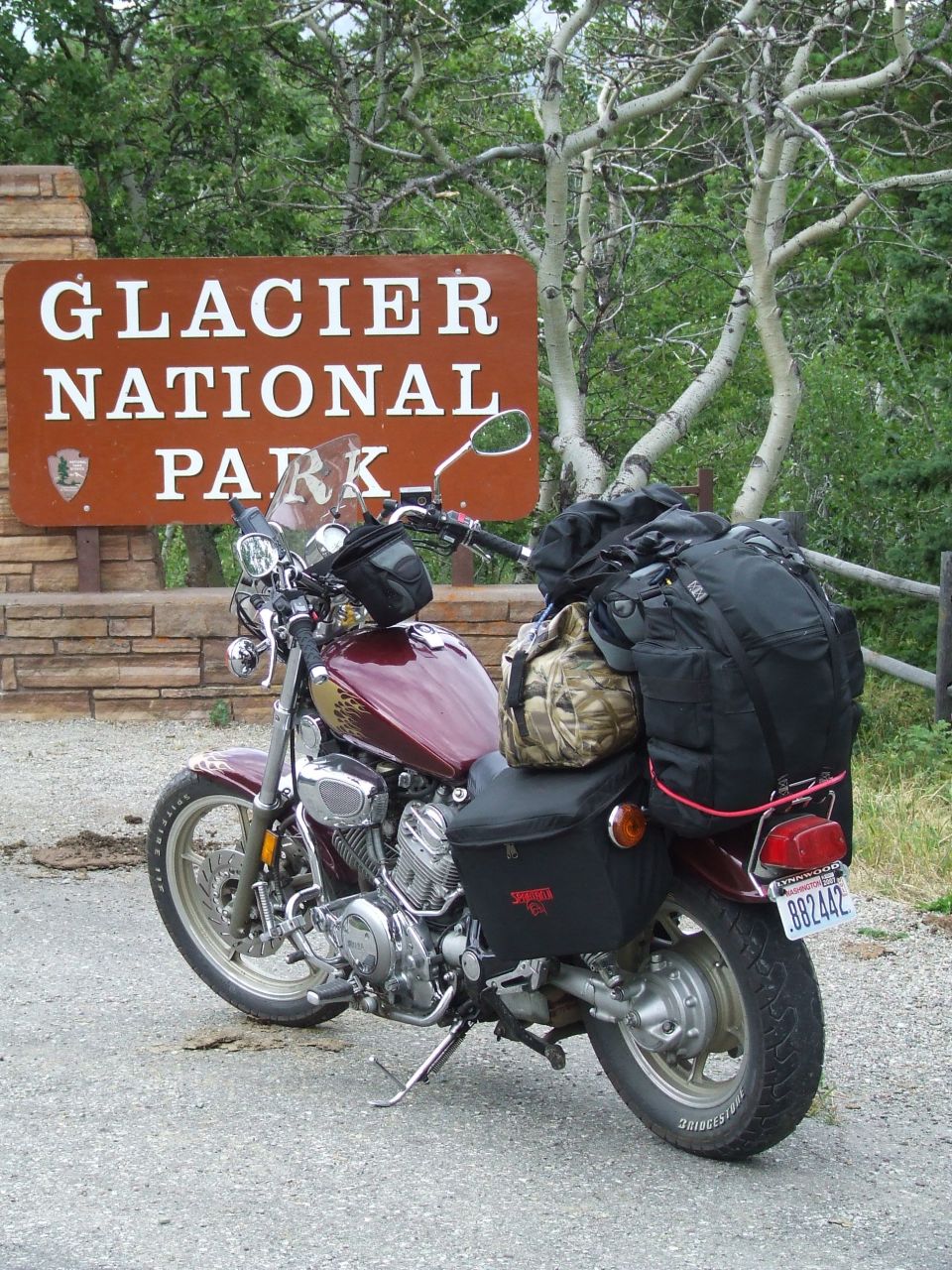 Maroon motorcycle with black saddlebags and luggage parked near a Glacier National Park sign