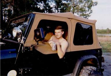 1986 Ford Bronco - Man leans out window of a tan soft-top Jeep Wrangler.