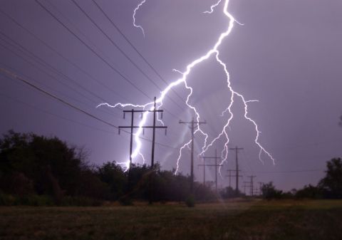 1979 Ford F-150 - A powerful lightning strike illuminates the sky over a line of utility poles and trees.