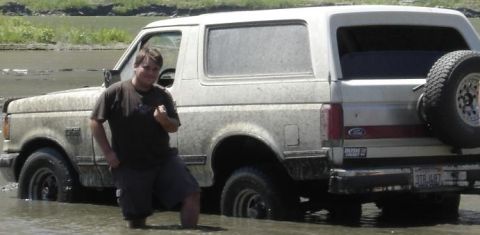 1988 Ford Bronco - A white Ford Bronco is stuck in shallow water, with a person standing next to it. The vehicle appears to be from the early 1990s.