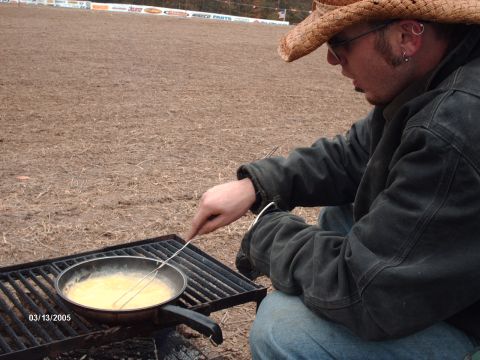 1995 Ford Probe - A man wearing a cowboy hat cooks eggs in a pan over a grill outdoors.
