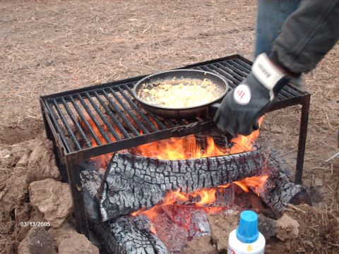 1995 Ford Probe - A person cooks food over a campfire using a frying pan and grill.