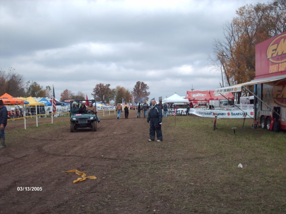 muddy field with tents, trailers, and people at an outdoor event. A utility vehicle is driving