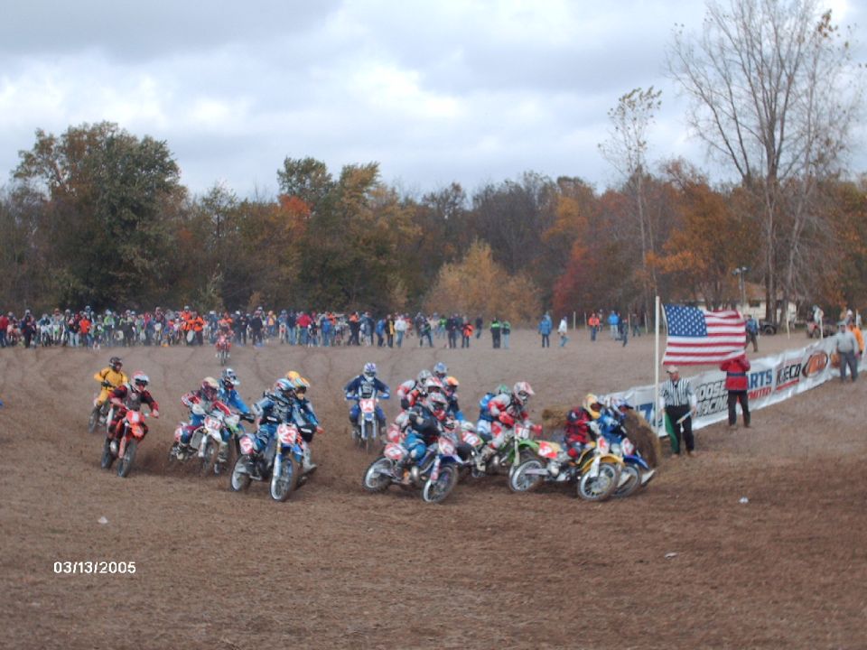 Motocross race start with many riders on dirt bikes, spectators in background, American flag flying