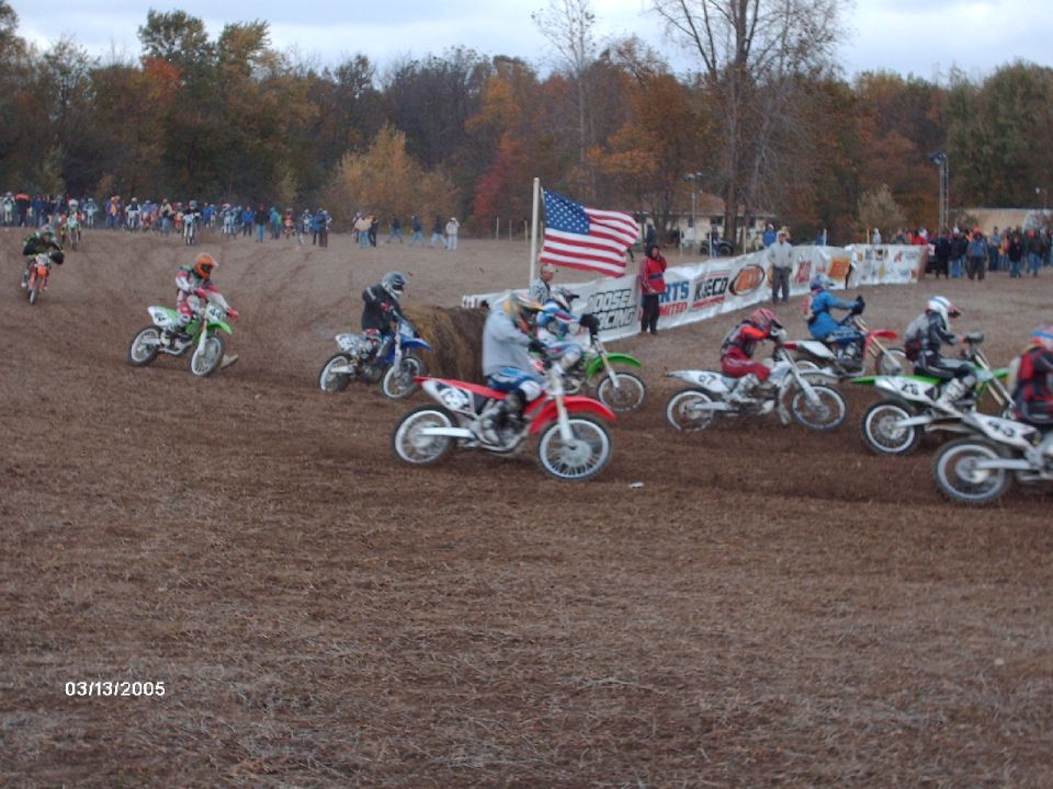 Dirt bikes racing on a track with spectators in the background and an American flag