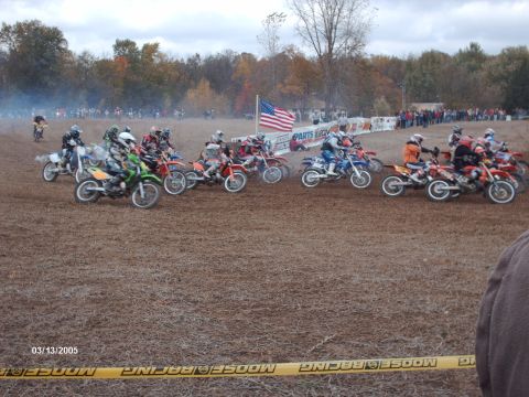 1995 Ford Probe - A group of dirt bikes and riders are lined up at the start of a motocross race, with spectators and trees in the background.