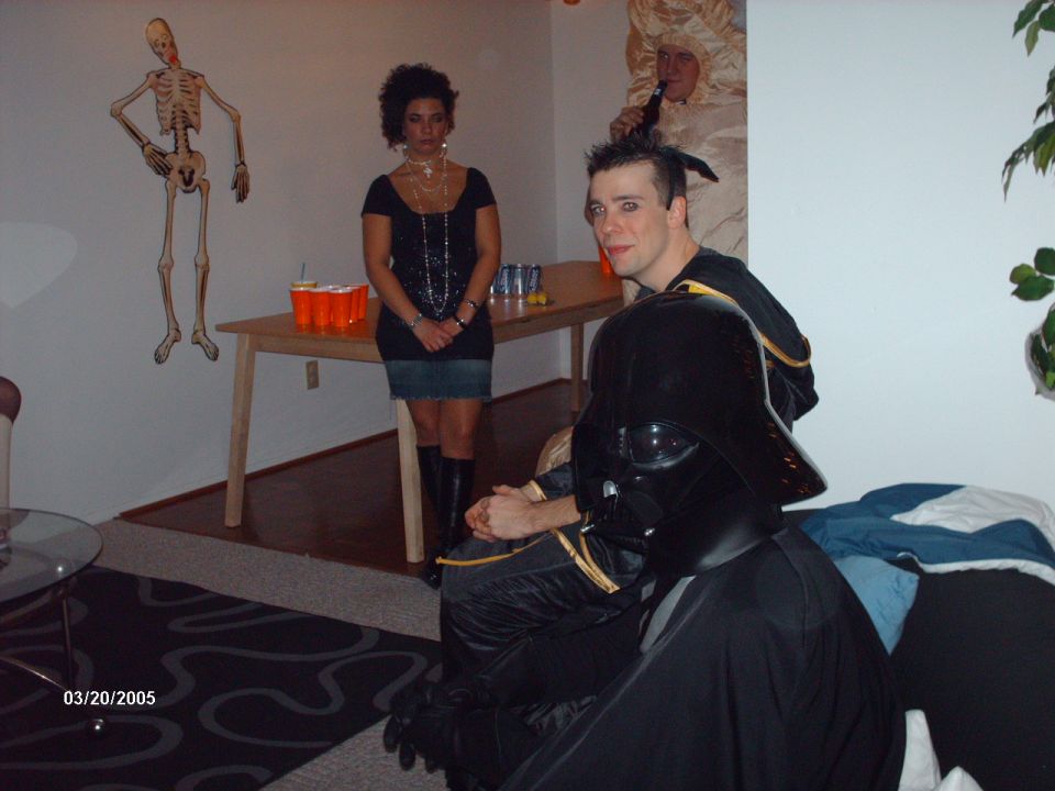 People in costumes, including Darth Vader, at a party with a skeleton decoration and orange cups on a table