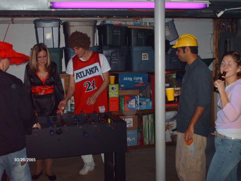 1995 Ford Probe - A group of friends gather for a game of foosball in a basement setting, with various items stored on shelves in the background.