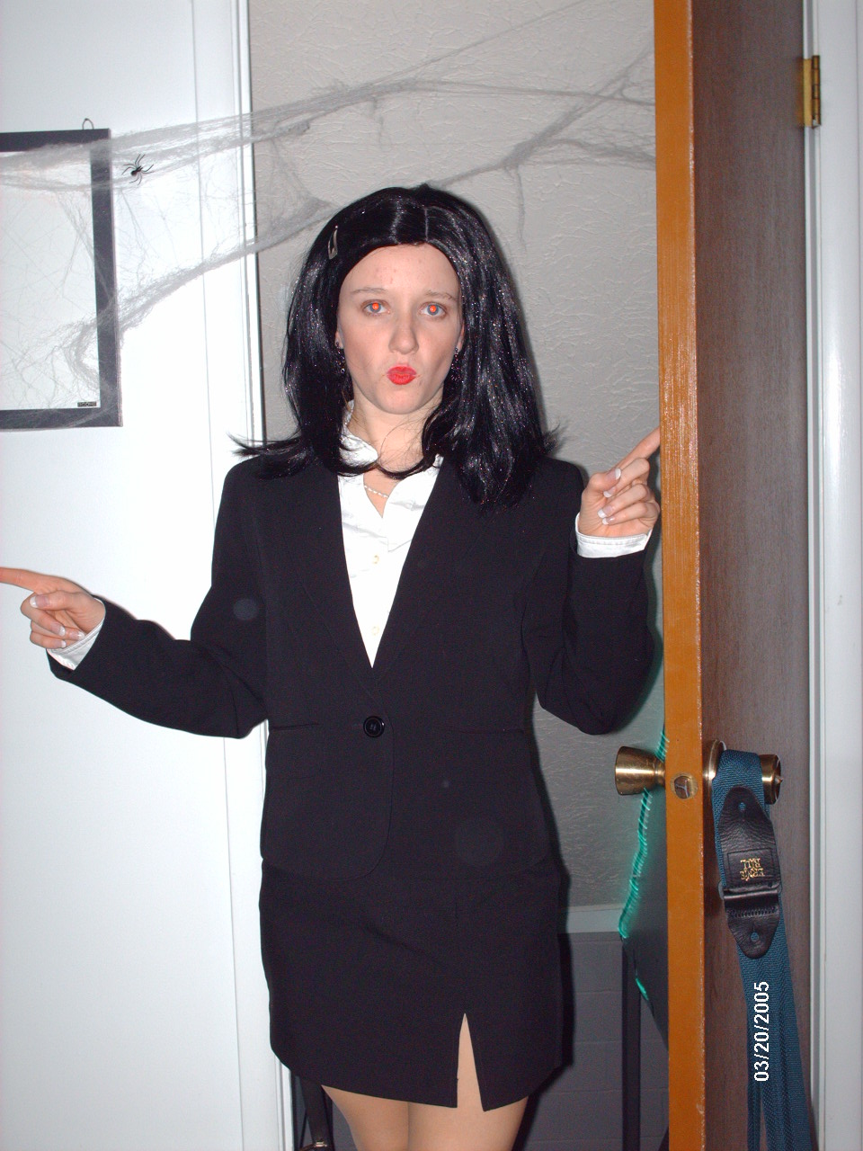 Woman in black suit and wig pointing, with fake spiderwebs