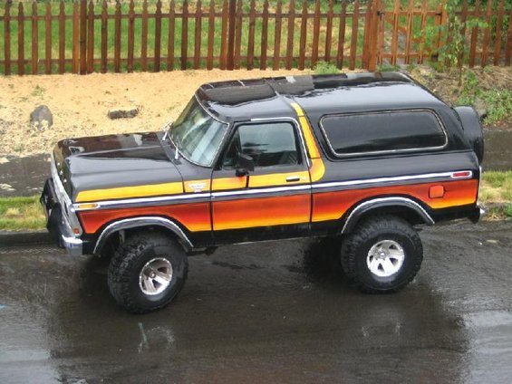 1978-1979 Ford Bronco with orange and yellow stripe graphics, parked on wet asphalt