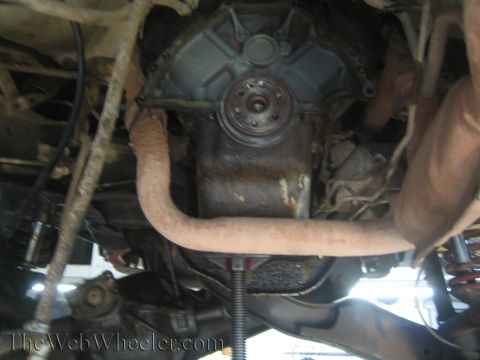 1990 Ford Bronco - Underbody view of a vehicle on a lift showing the front differential housing, exhaust crossover pipe and suspension links.