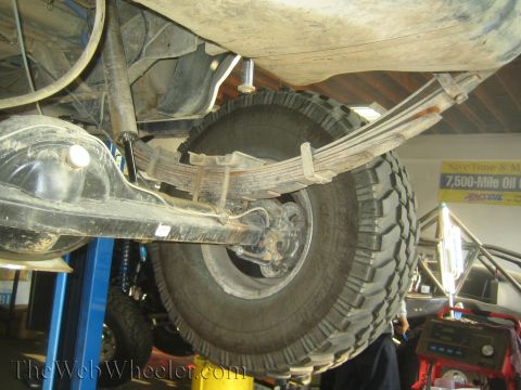 1990 Ford Bronco - Undercarriage of a lifted truck showing the rear leaf spring, differential housing, and a mounted off-road tire.