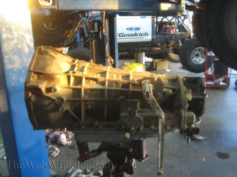 1990 Ford Bronco - Side profile of a removed transmission housing on a jack, backlit, with a BFGoodrich sign in the shop behind it.