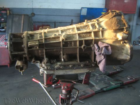 1990 Ford Bronco - full automatic transmission rests on a hydraulic jack with a rag draped over the tailshaft end in a repair shop.