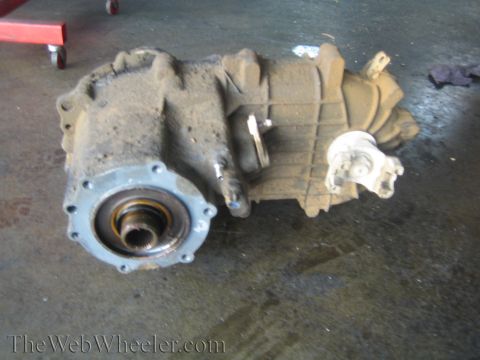 1990 Ford Bronco - cast transfer case sits on a shop floor, showing its splined front output bore and rear output yoke.