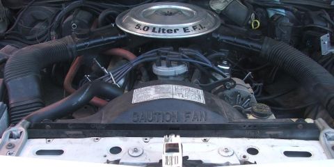 1985 Ford LTD Crown Victoria - Engine bay of a white Ford sedan with the hood up, showing a V8 topped by a round chrome air cleaner lid stamped '5.0 Liter E.F.I.', the di…