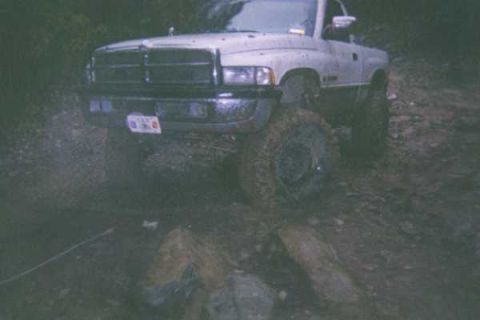 1978 Ford Bronco - A white pickup truck is stuck in the mud, its large tires covered in dirt.