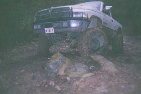 1978 Ford Bronco - A white pickup truck is stuck in the mud, its front end visible with large tires.