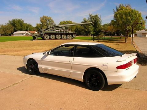 1993 Ford Probe - A white 1993 Ford Probe GT is parked on a paved surface with a military tank in the background.