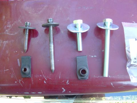 1990 Ford Bronco - A collection of bolts and U-nuts are laid out on a red surface, possibly for a vehicle repair.