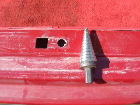 1990 Ford Bronco - A step drill bit rests beside two freshly drilled holes on a red metal surface.