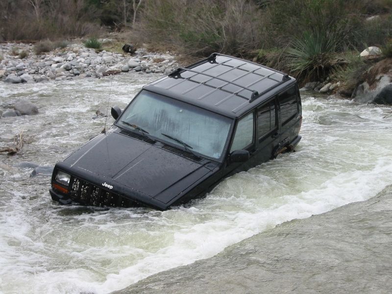 Black Jeep Cherokee XJ stuck door-deep in a fast-flowing rocky river