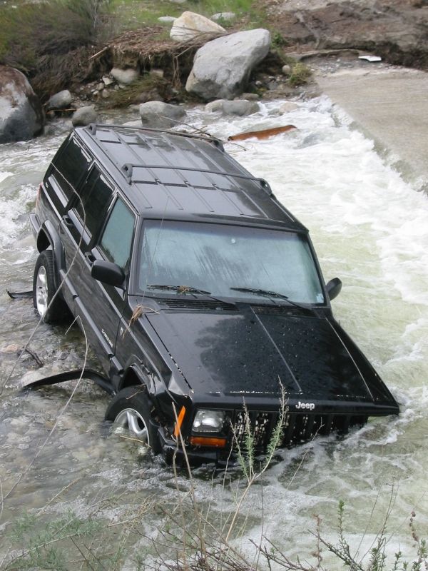 Black Jeep Cherokee nose-down in a rushing river with water washing over the front bumper