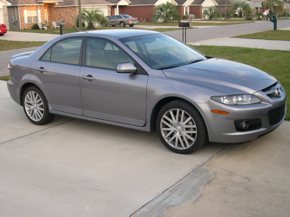 Gray sedan parked on a concrete driveway, front quarter view. The car has alloy wheels and appears to be in good condition