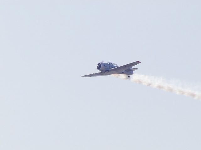 Vintage single-engine prop warbird banking against gray sky trailing smoke